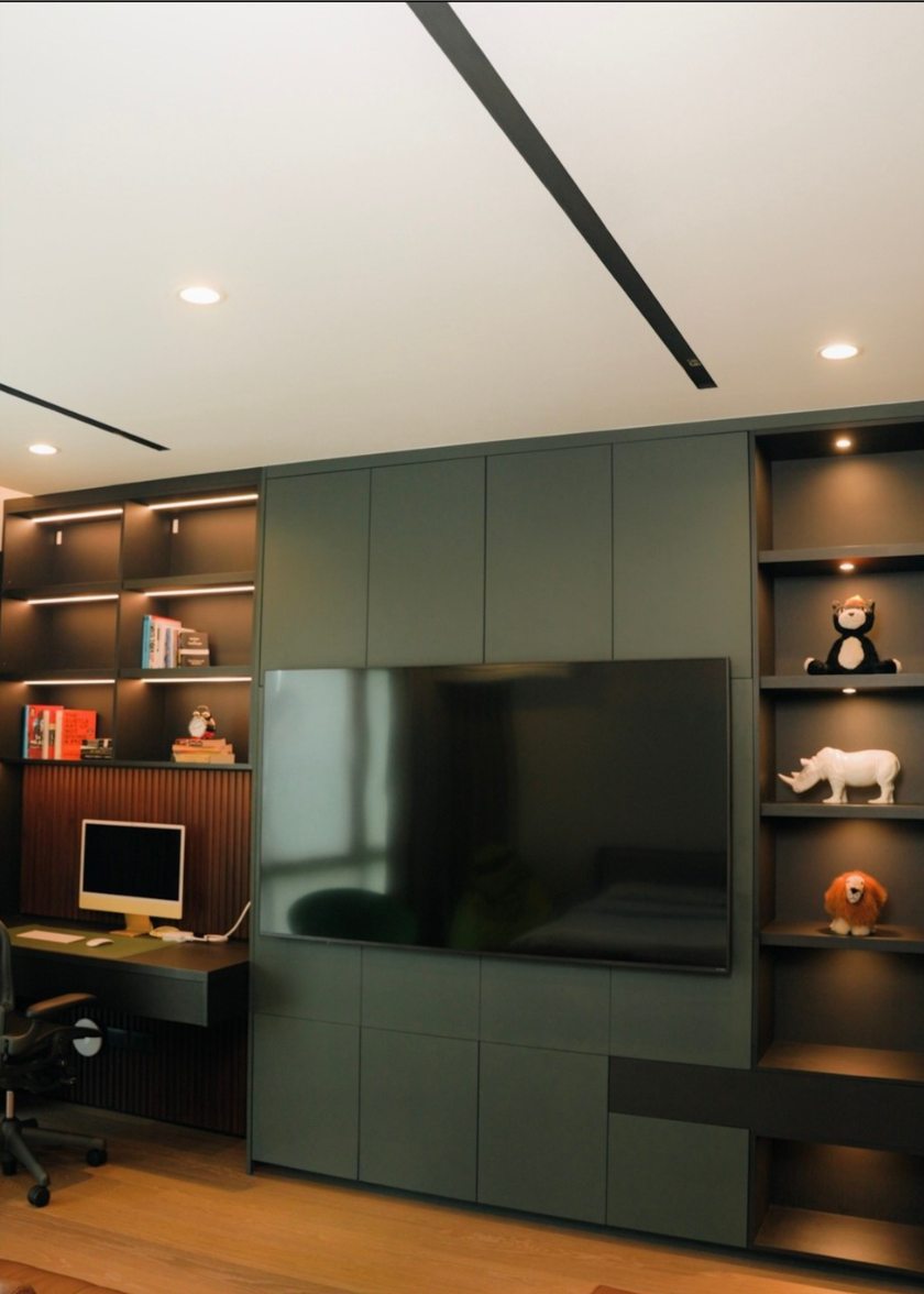 Full-height olive cabinetry integrating a television, work desk, and illuminated shelving
