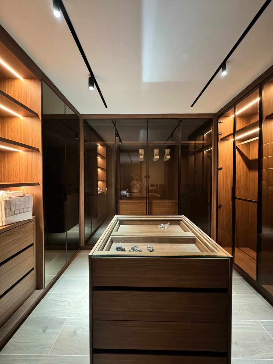 Walk-in closet with smoked glass doors, walnut storage, and a central island